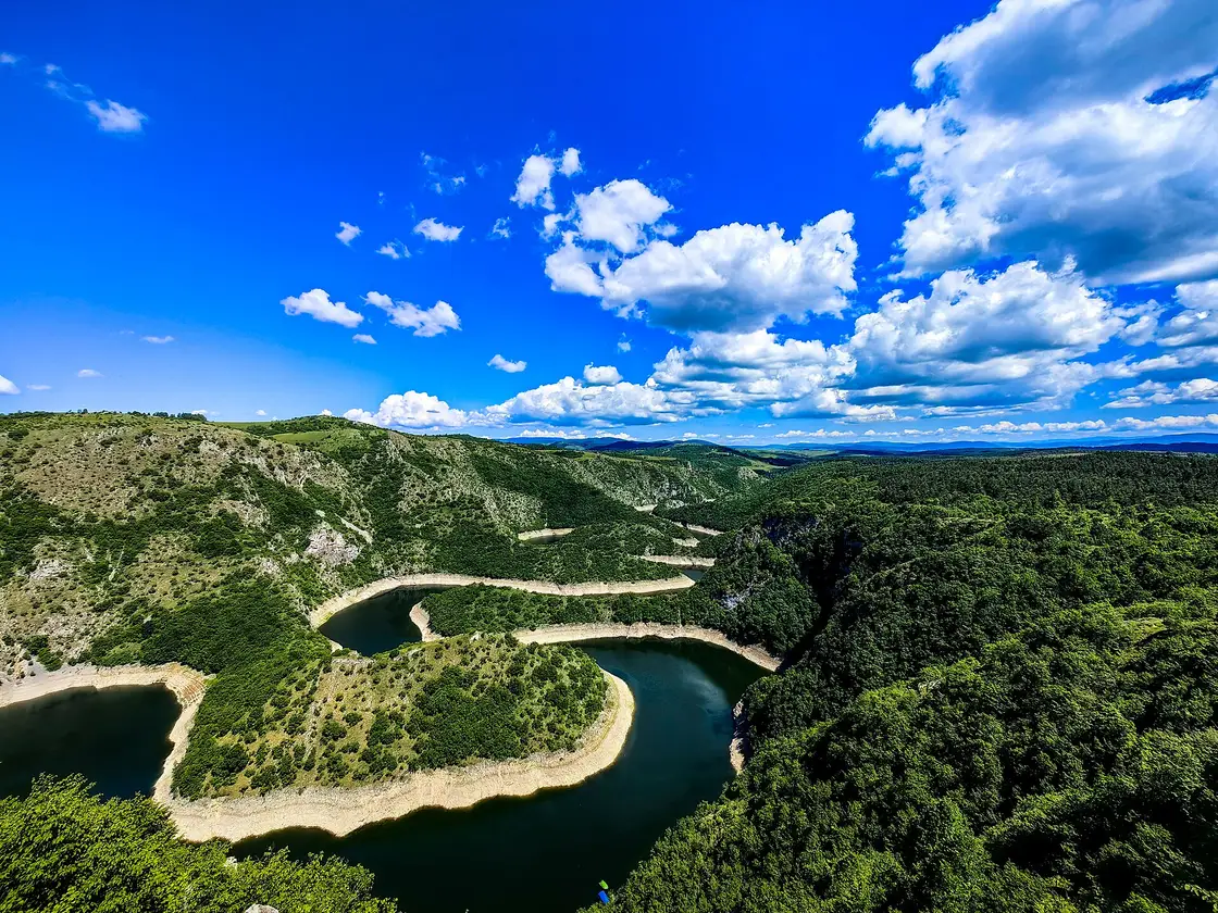 A tight green meander of the Uvac far below the Veliki Vrh viewpoint under a blue summer sky