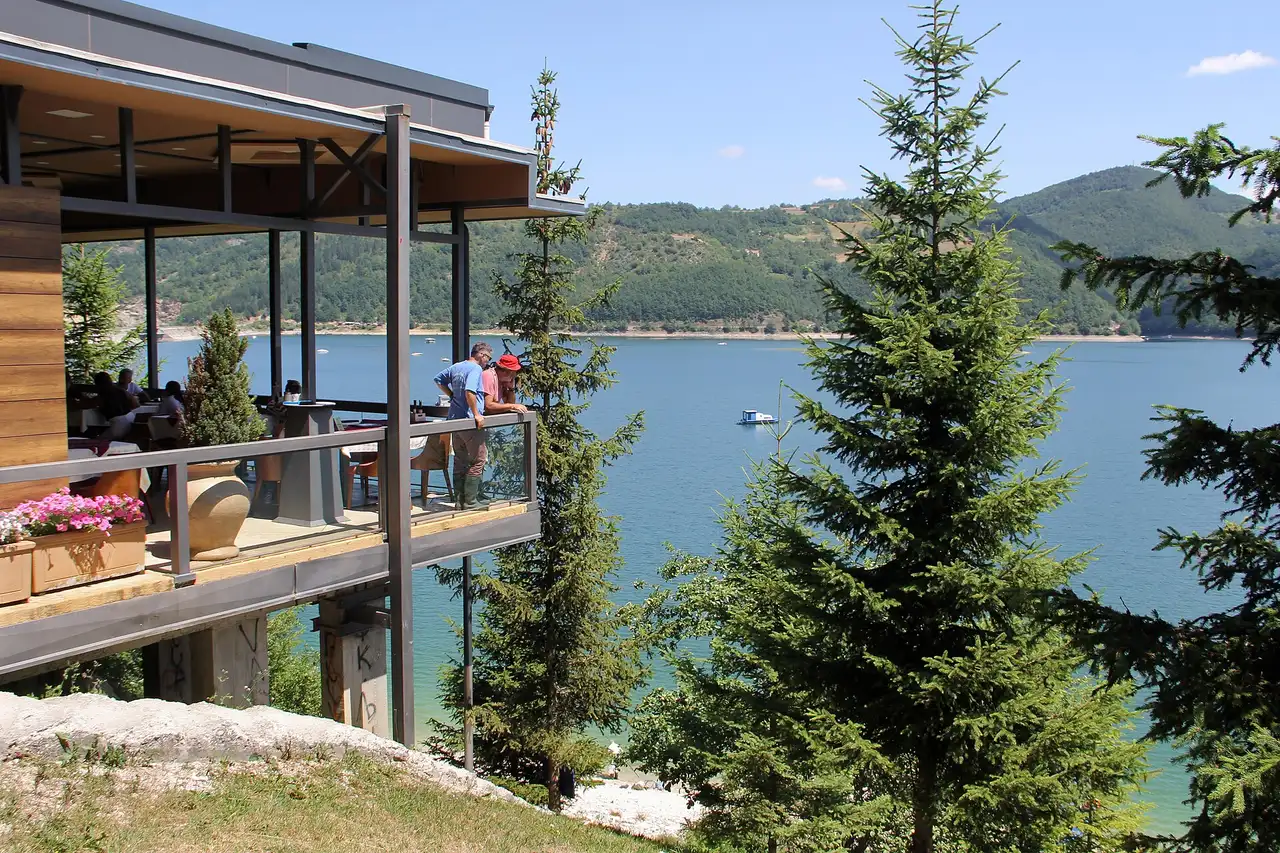 A lakeside terrace above the green water of Zlatar lake at Kokin Brod with a small boat crossing behind