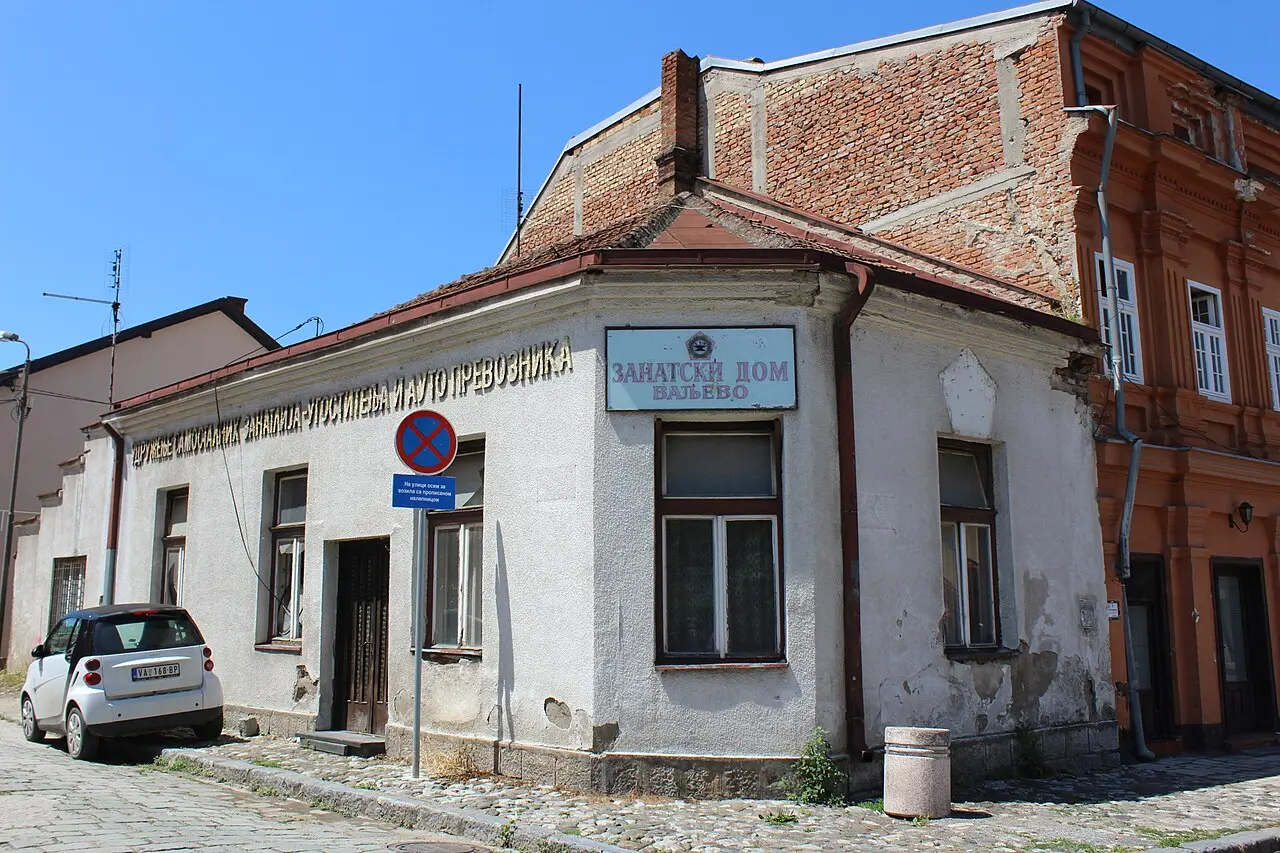 Zanatski Dom on Tesnjar, craft-association signs and a Smart parked on the cobbles