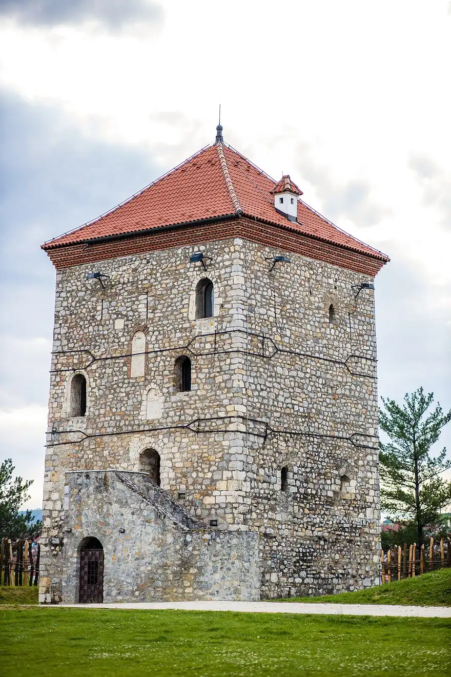 The stone Nenadovic Tower in Valjevo with a red tiled roof and small arched windows, seen against a cloudy sky