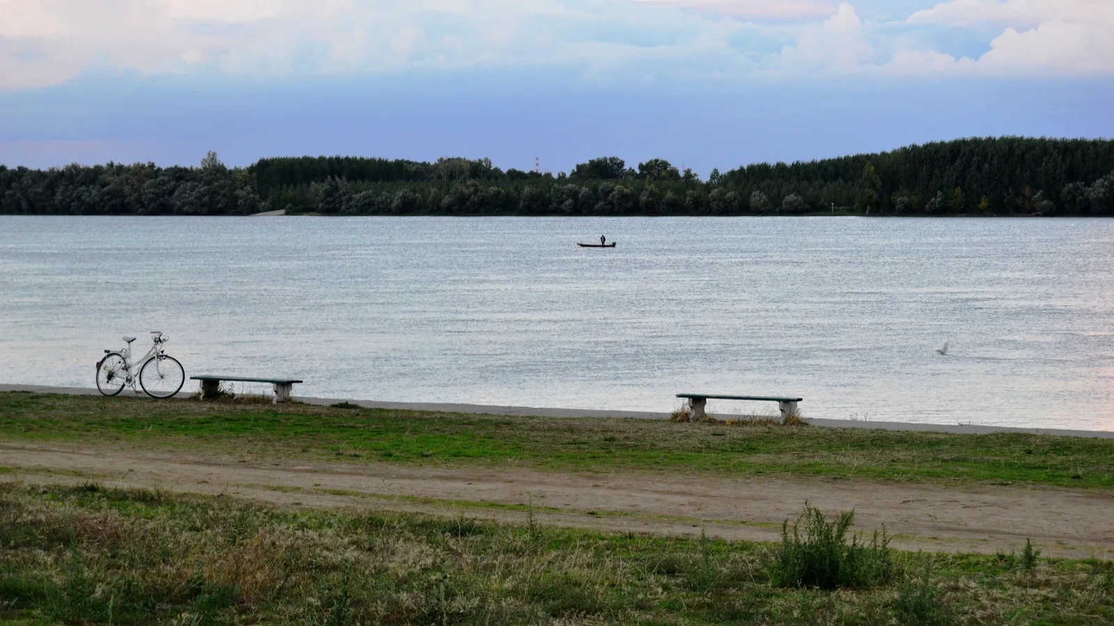 A quiet stretch of the Danube riverbank near Vinca village at dusk, with a bicycle and stone benches on the path