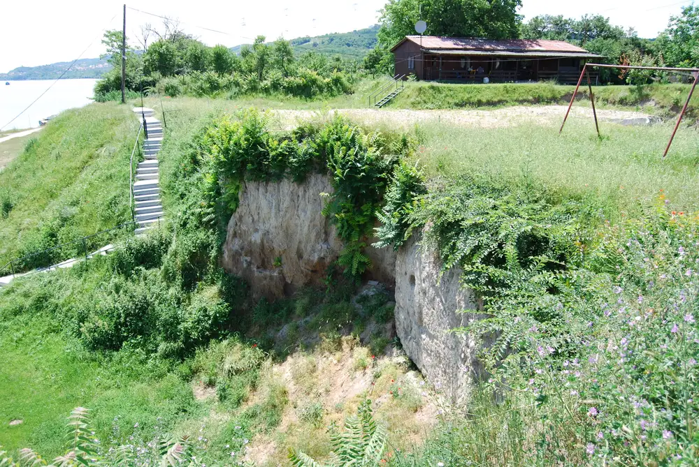 The eroded earthen profile of the Belo Brdo mound at Vinca, cut back near the Danube riverbank with stairs leading down beside it