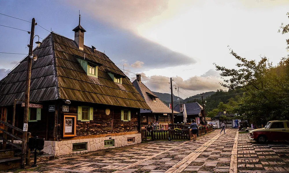 The wooden shingle-roofed houses and cobbled street of Drvengrad, the timber village Emir Kusturica built above Mokra Gora, at golden hour