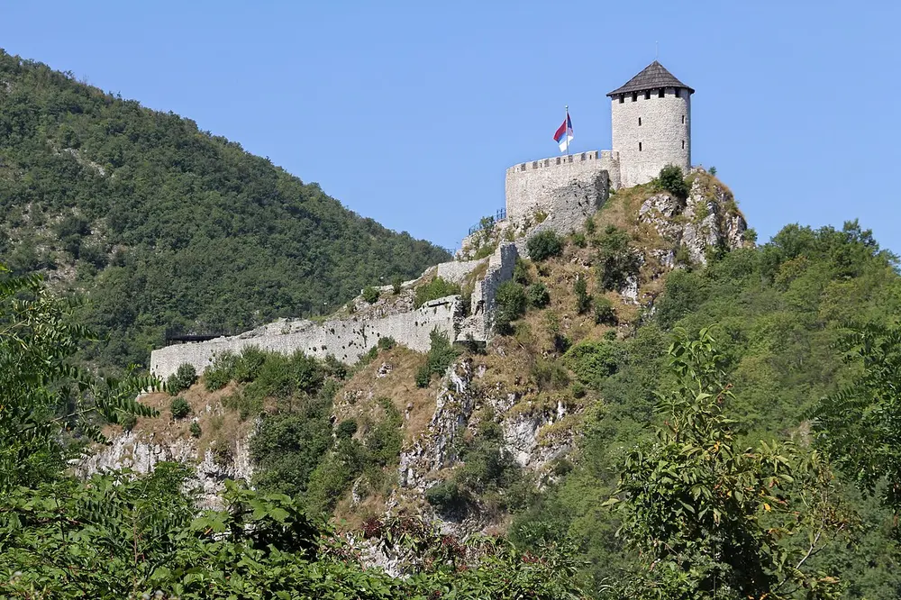 The stone tower and walls of Uzice fortress standing on a cliff above the Detinja gorge, with a Serbian flag flying