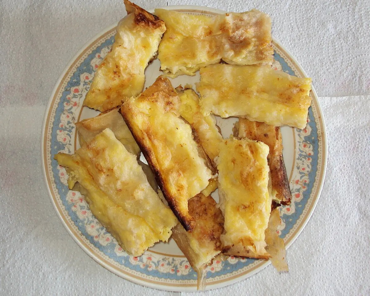 A plate of golden baked gibanica, a layered filo and white cheese pie, cut into pieces