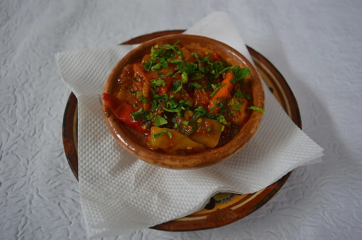 A rustic clay bowl of pinđur, a cooked red pepper and tomato spread, topped with chopped parsley