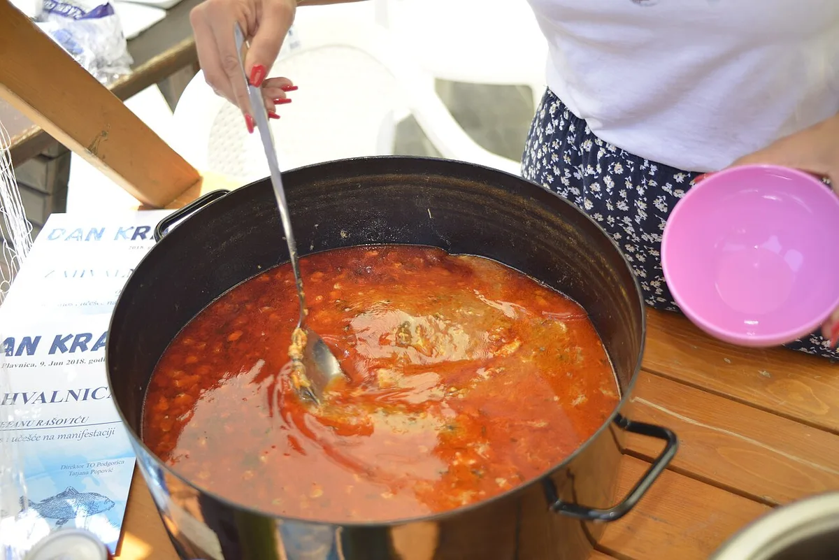 A large cauldron of red riblja čorba fish soup being ladled out at a Danube carp festival