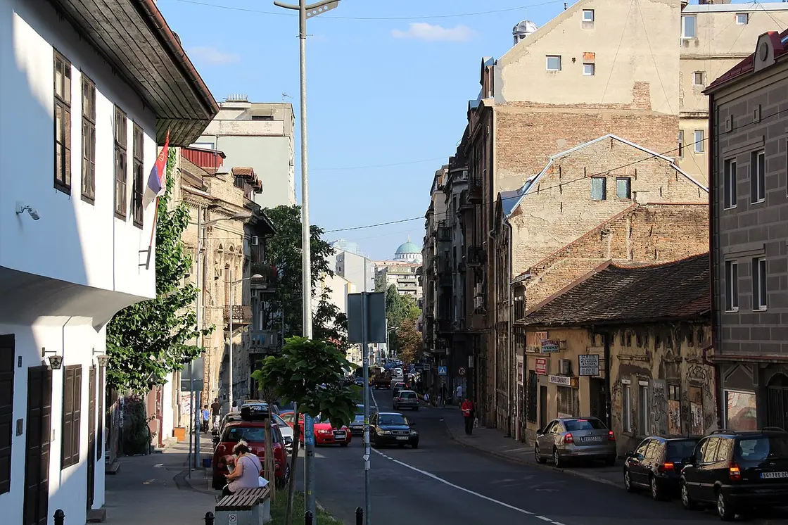 A sloping central Belgrade street in the Savamala area with mixed old buildings and the St Sava dome behind